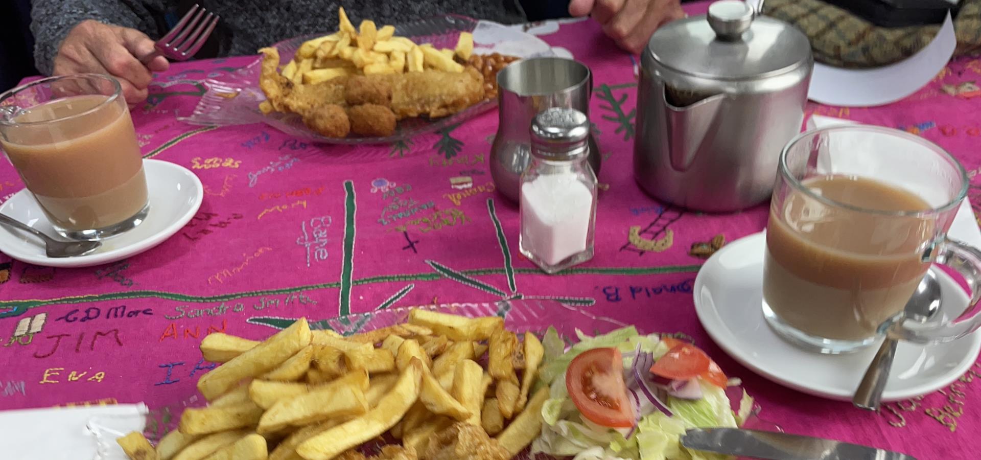 A table with the tablecloth, two cups of tea and two plates of food
