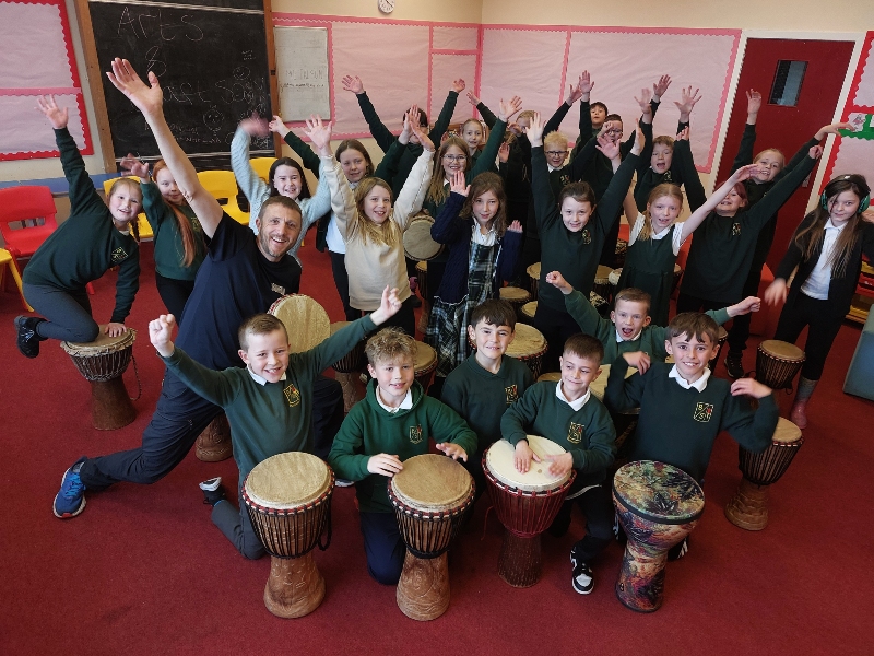 group of primary school children with drums posing with hands up in the air