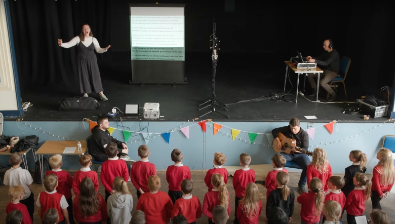musician on stage conducting a large group of children singing