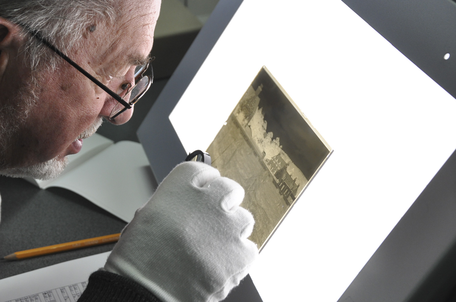 Gentleman looking closely at a glass negative on a lightbox.