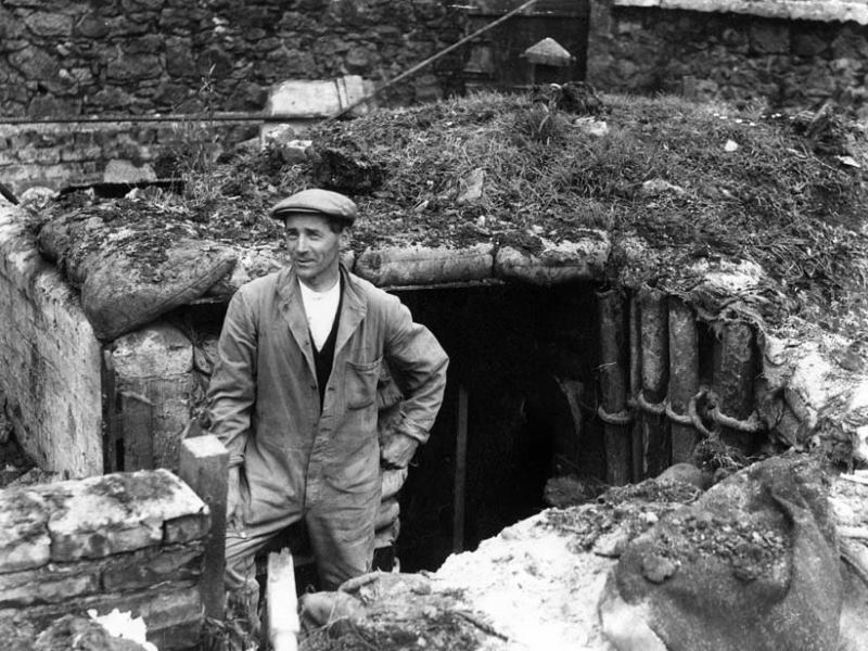 A Peterhead gentleman stands at his homemade dugout air raid shelter. With sandbags and earth forming its roof.