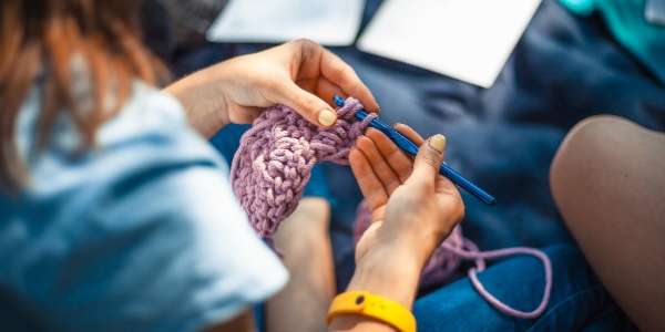 Person crocheting a scarf with purple wool