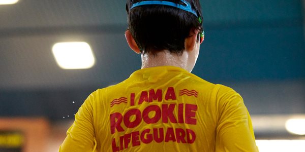 A young person wearing a yellow t-shirt with the words I am a rookie lifegaurd