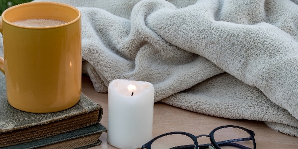 a blanket, candle, pile of books and cup of tea