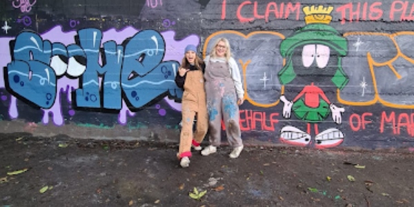 Some street art on a wall with the artists standing in front