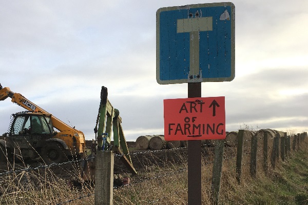 A digger in a field next to a sign showing the Art of Farming is straight ahead